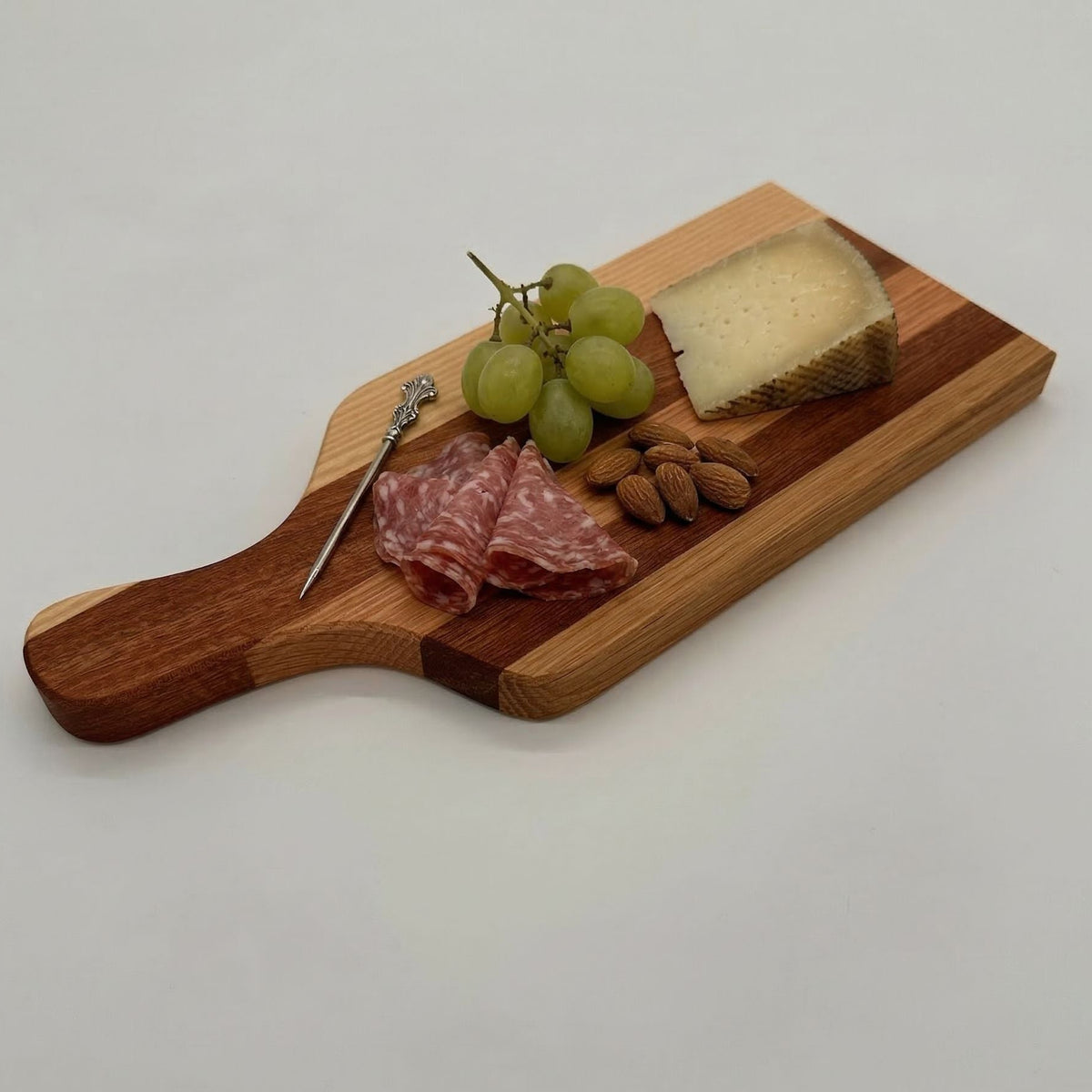 Wooden cutting board with salami, grapes, and cheese on a white background