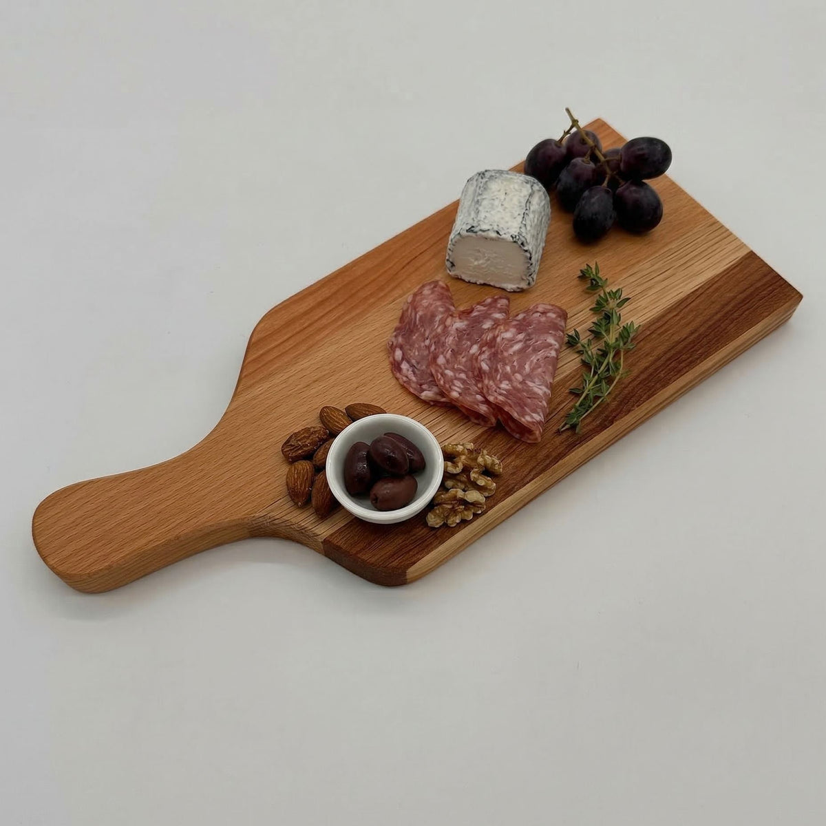 Wooden cutting board with cured meats, cheese, grapes, and olives on a light gray background