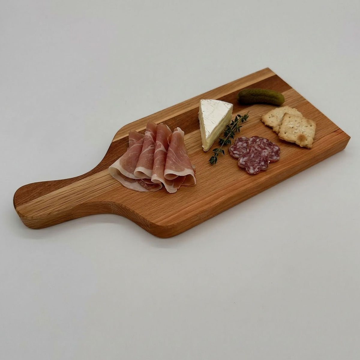Wooden charcuterie board with cured meats, cheese, and bread on a light gray background