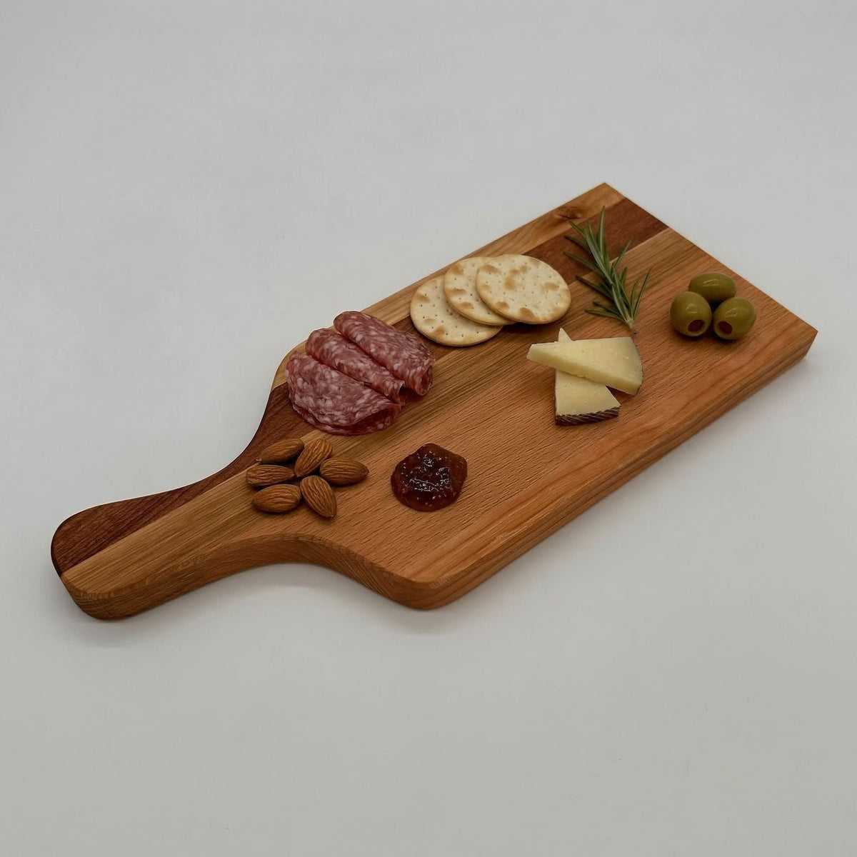 Wooden charcuterie board with salami, crackers, cheese, olives, and nuts on a white background