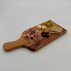 Wooden cutting board with cured meat, cheese, grapes, and crackers on a white background