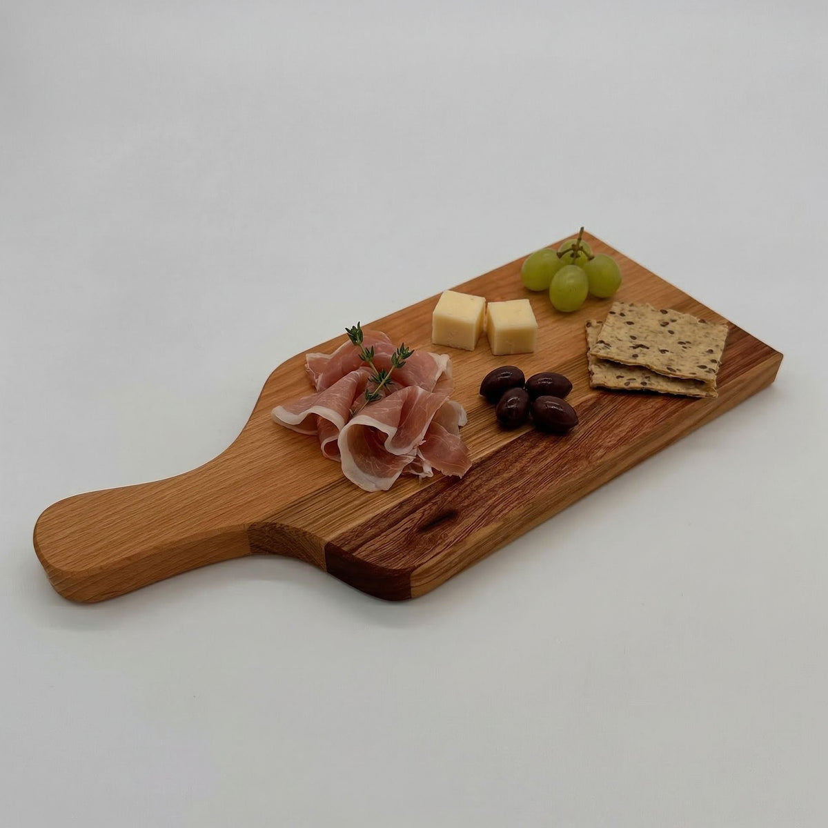 Wooden cutting board with cured meat, cheese, grapes, and crackers on a white background