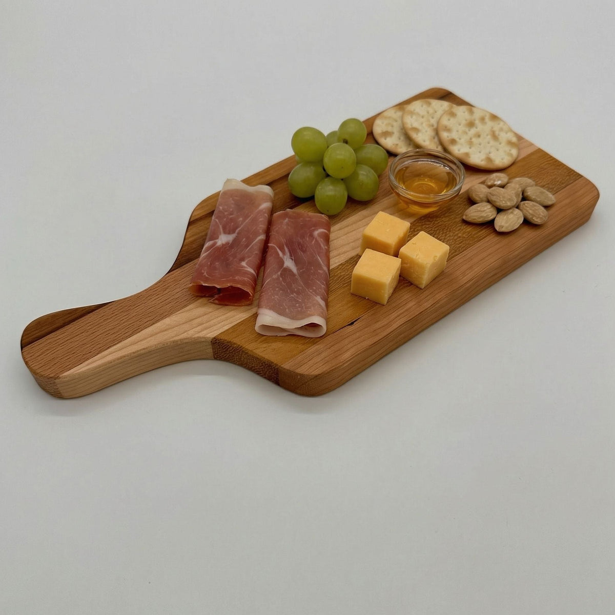 Wooden cutting board with cured meats, cheese, grapes, and nuts on a white background