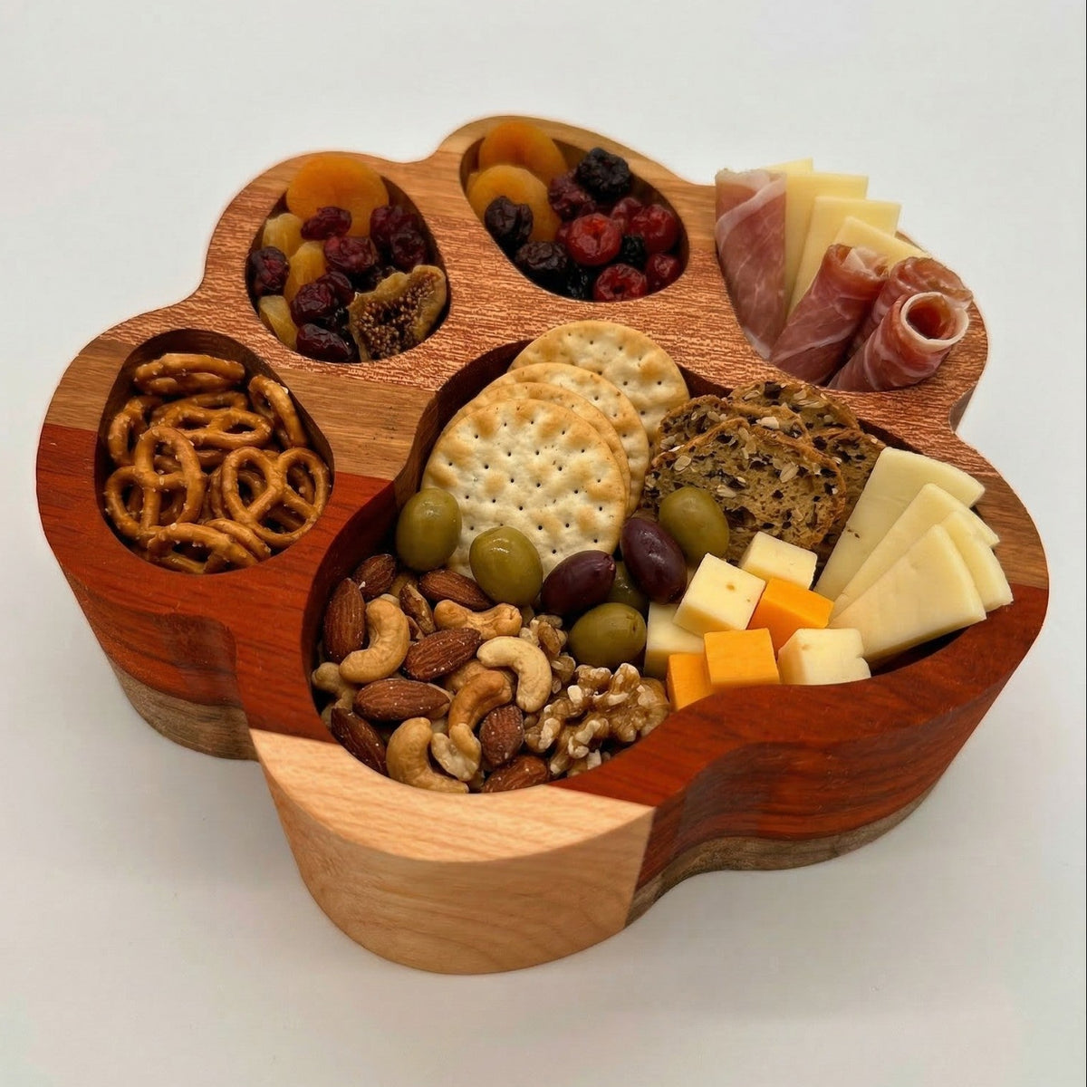 Wooden snack board with various foods including cheese, fruits, and nuts on a white background