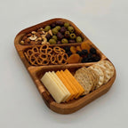 Wooden snack tray with cheese, crackers, and assorted snacks on a white background