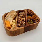 Wooden snack tray with crackers, cheese, nuts, and fruits on a white background